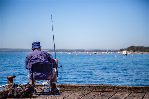 Seated man fishing from a pier